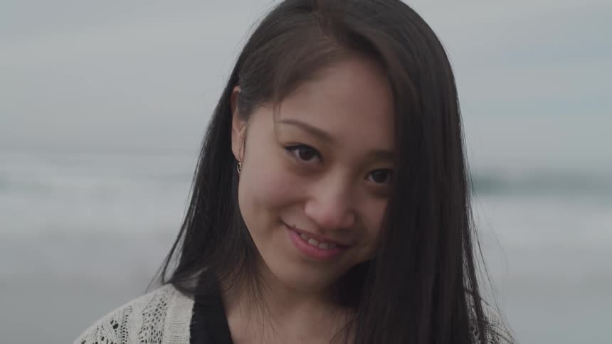 A young woman at the beach looks into a camera and smiles