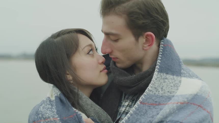 A young couple huddle in a blanket and kiss