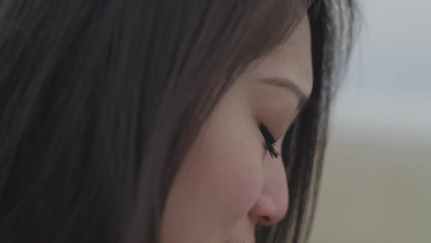A woman looks into the distance then looks down and covers her mouth with her hand
