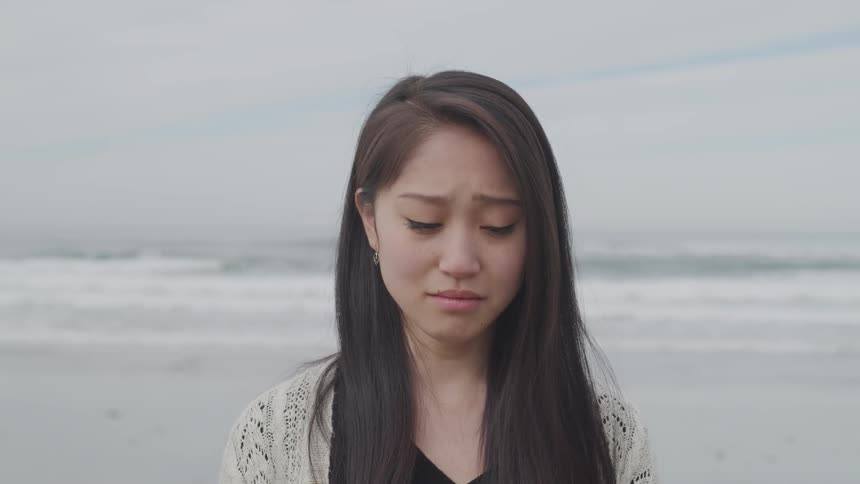 Woman sheds tears on the white beach next to the sea during daylight