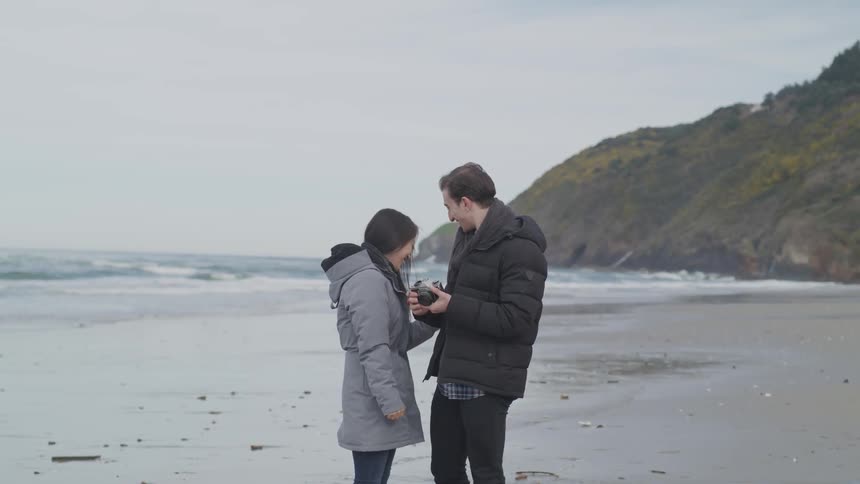 A man and a woman look at a camera on the beach