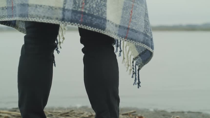 A person stands on a beach wearing a blue blanket