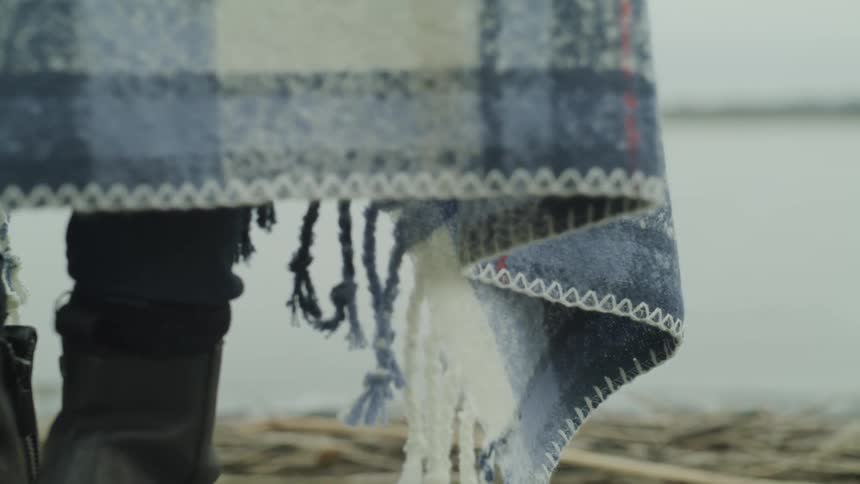 A person draped in a blanket standing on the beach