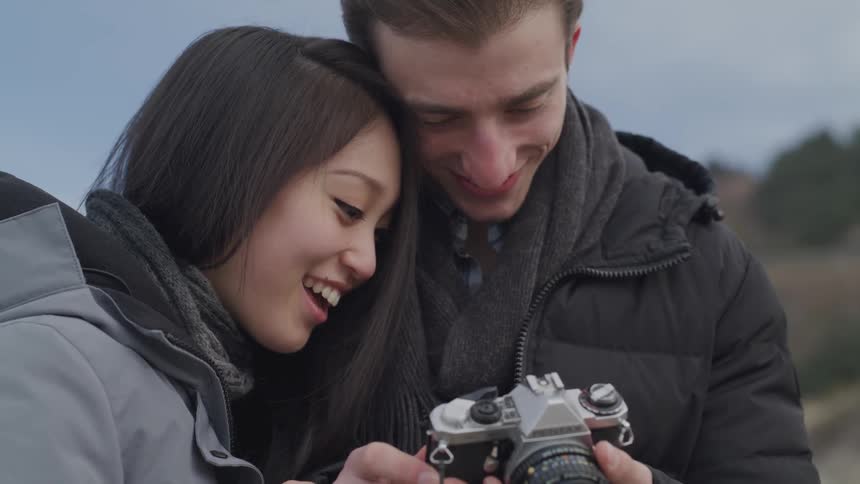 A young couple look at a camera and smile to one another