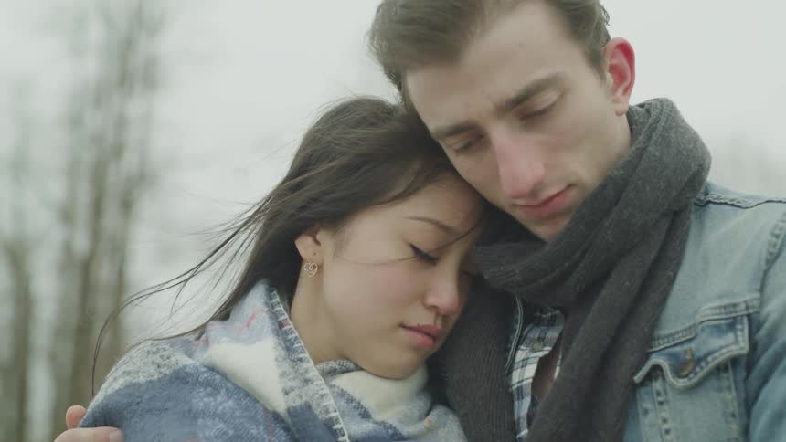 A man hugs a woman who is leaning her head on his shoulder as a breeze blows her hair
