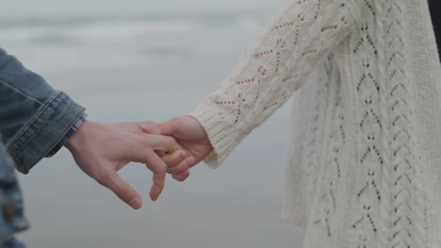 A man and woman hold hands while walking outside
