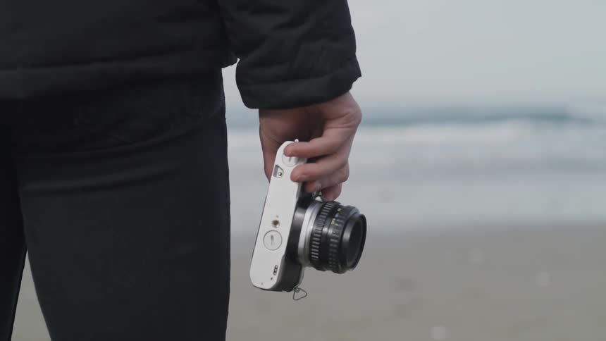A person stands looking out at the ocean with a camera in their hand