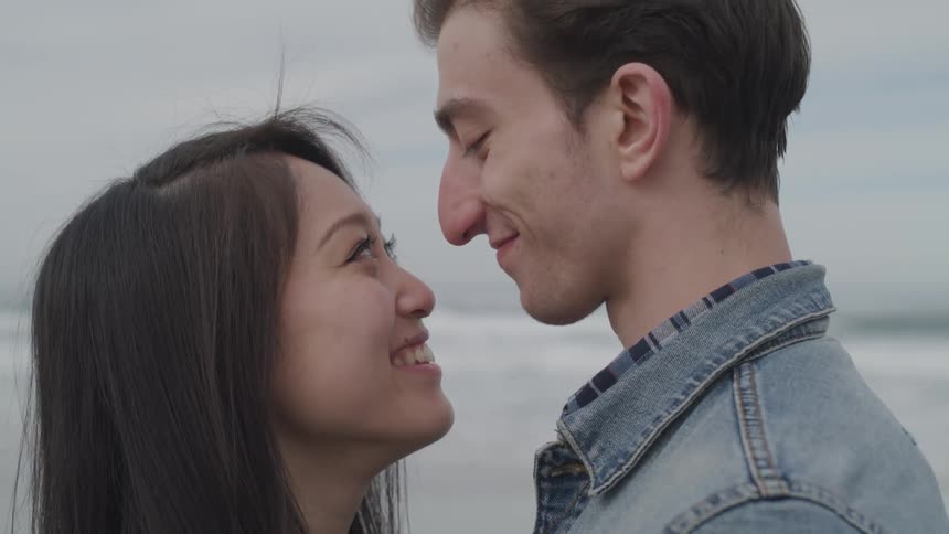 A man and woman look into each others eyes while standing on a beach