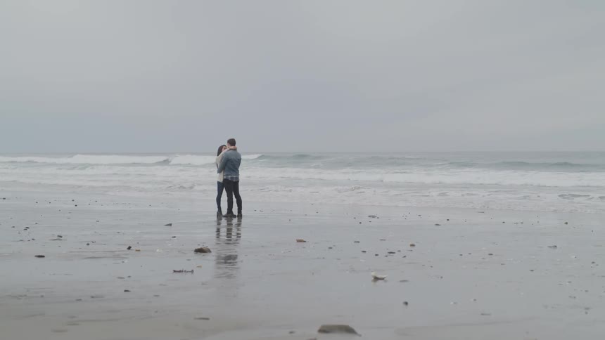 A man and woman embracing on a beach on a cloudy day