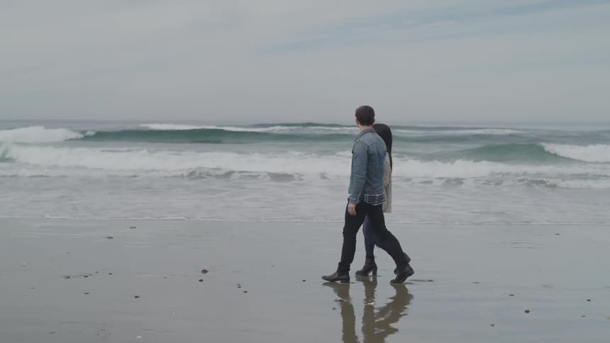 A man and a woman walking on the beach