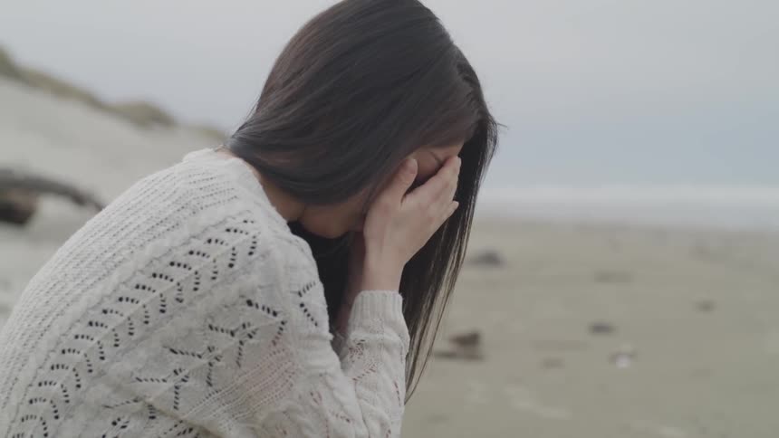 Asian female wearing a sweater looking nervous while sitting on the beach