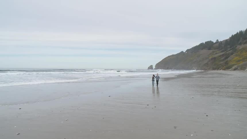 A woman and man walk along a beach while holding hands