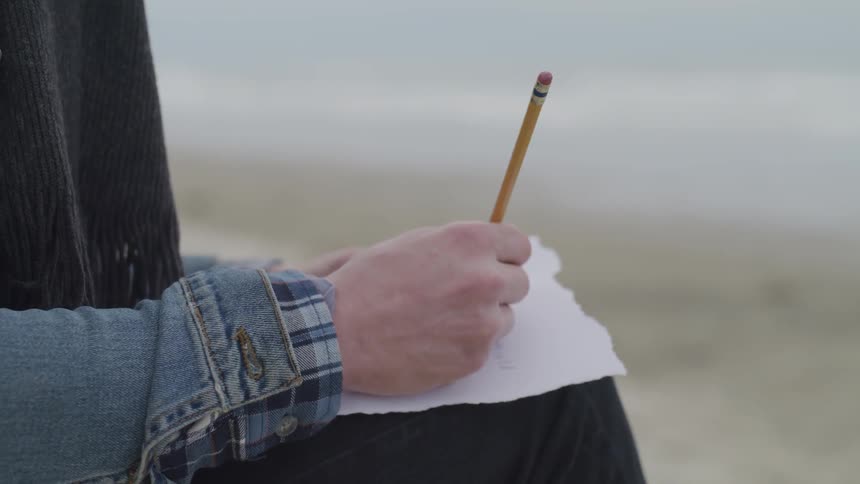A person writing on a piece of paper with a pencil