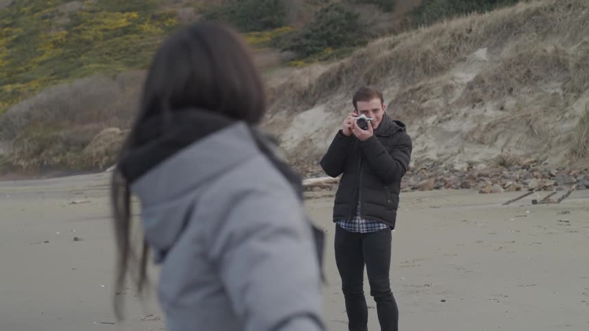A man in skinny jeans takes photos of a woman in a winter coat