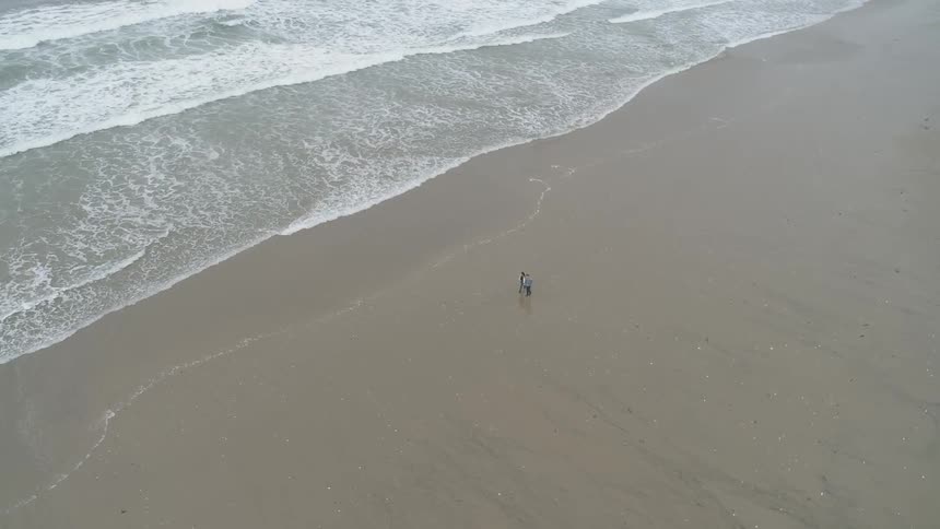 Two people walks on the beach while waves hit the shore
