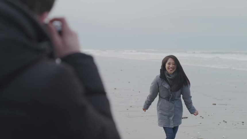 A man photographs a smiling woman on a sandy beach