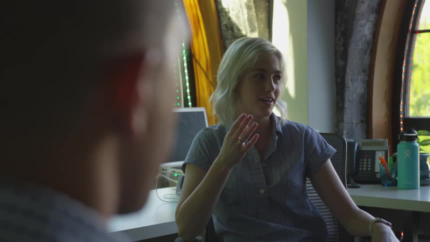 A woman sits at her desk while talking with others