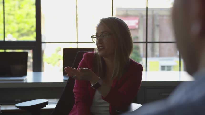 Two women and a man chat during a meeting near a large window