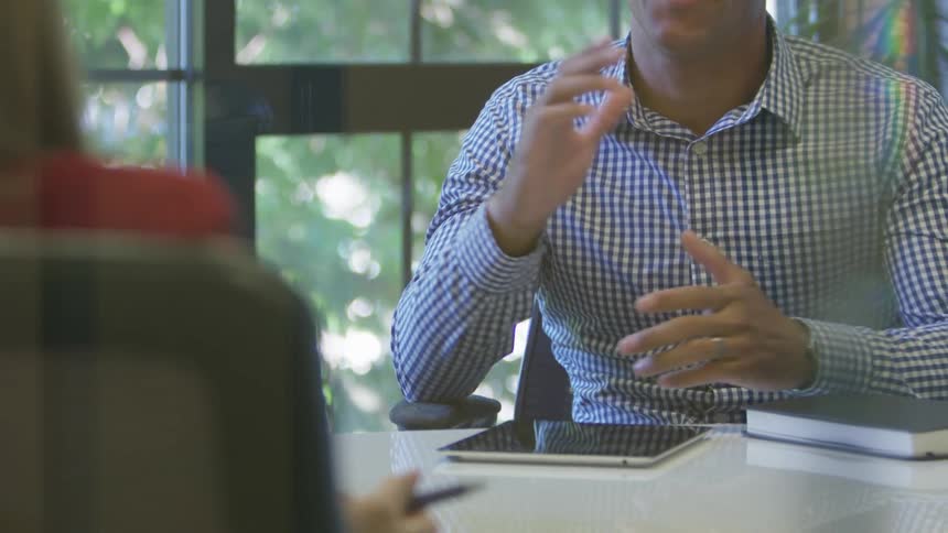 A man sits at a conference table and talks to a woman across from him