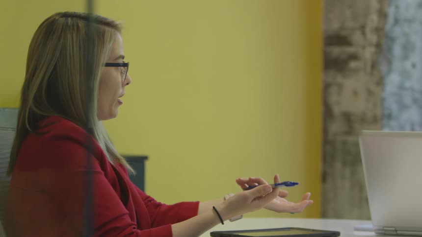 A woman is talking in a conference room while moving her hands and touching a pen