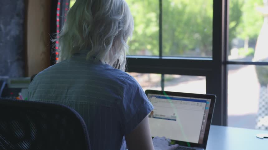 A woman works on a laptop at a desk by the window