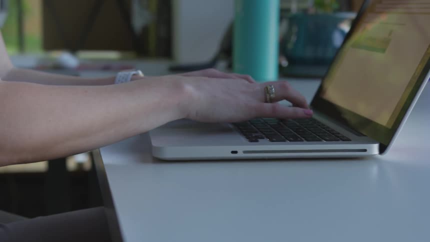 Woman types on a laptop that is resting on a desk