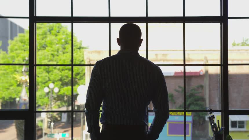 Silhouette of a male looking out the window overlooking a neighborhood