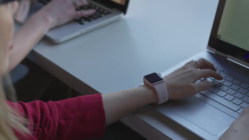 A woman types on a laptop while wearing a smartwatch