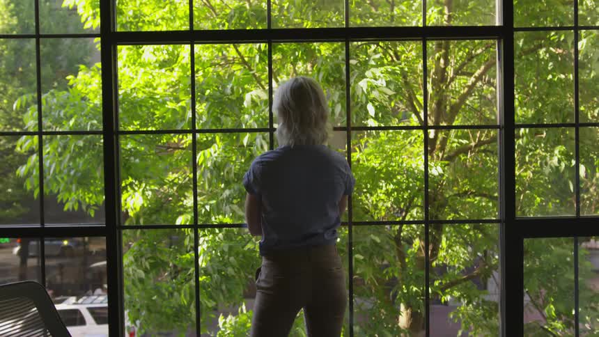 Woman stands in front of large window looking out
