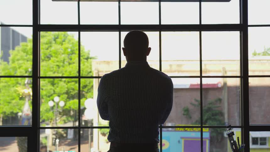 A man crosses his arms and looks out a large window