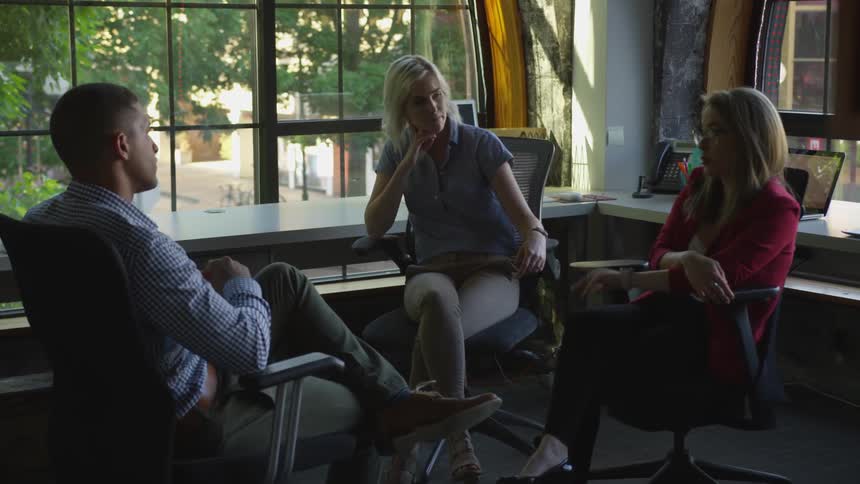 Two women and man sit in chairs and have a conversation in the corner of the room during daylight