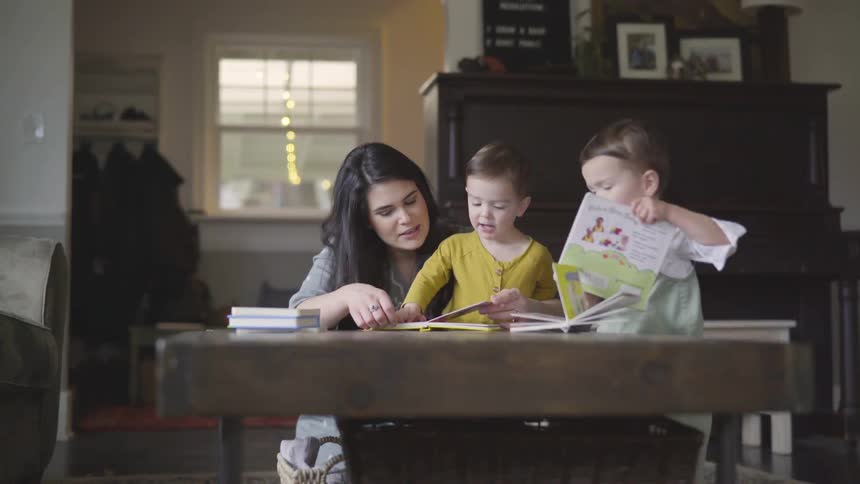 Woman shows books to the two children at home during daytime