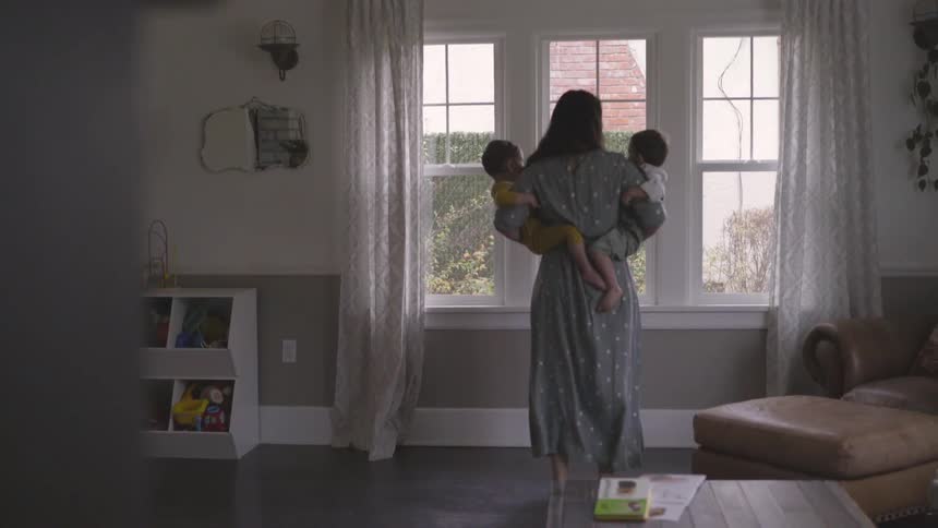 A woman holding young children in each arm while standing in the house in her robe