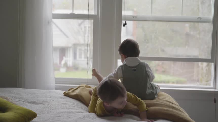 Two toddlers sit on the bed and play together on a cloudy day