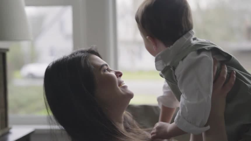 Mother lifting baby up and down while playing on the couch