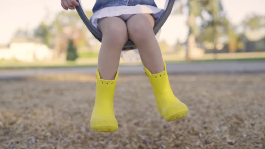 A young girl in yellow rubber boots sitting on a swing