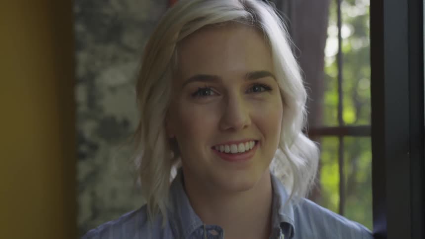 A woman standing next to a windows smiling and looking towards the camera
