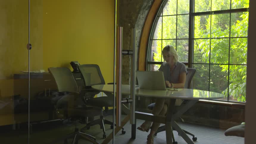 A white woman sits in an office while using a laptop