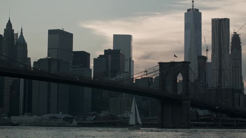 View from the water of a sailboat, bridge and city skyline under a cloudy sky