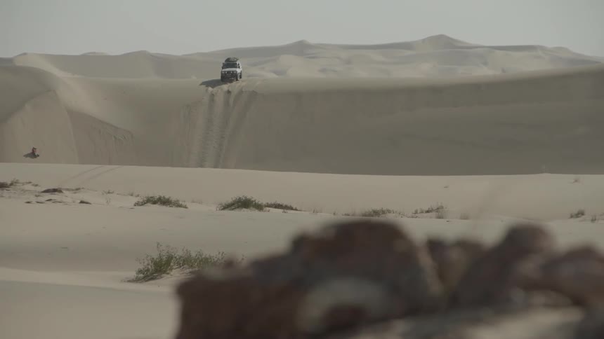 Three suv descend down a sand dune in the desert