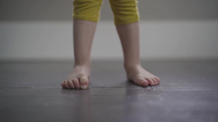 Bare feet toddler stands on the concrete ground during daytime