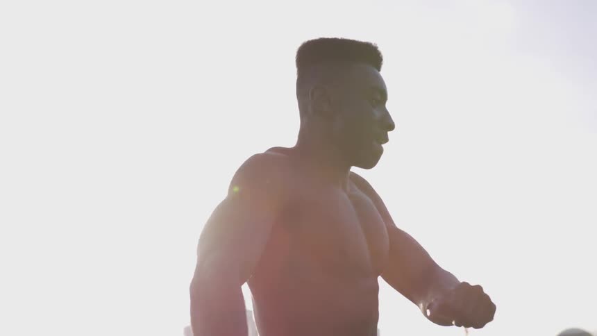 Shirtless, muscular black man warms up outdoors while sun shines on his skin