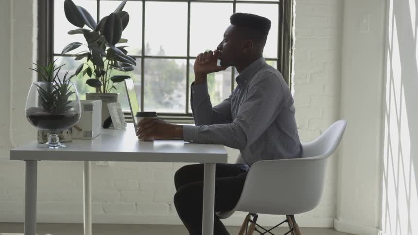 Male sitting at table near a window reading on his laptop