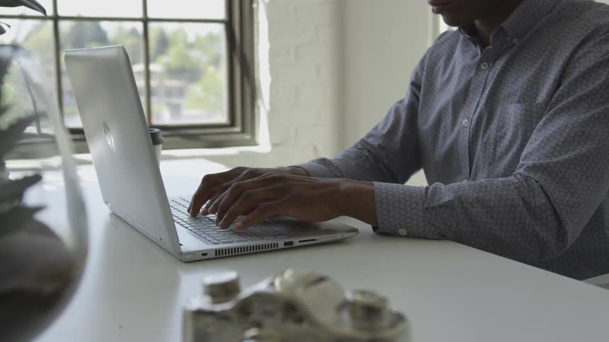 A man is sitting at a table typing on a laptop