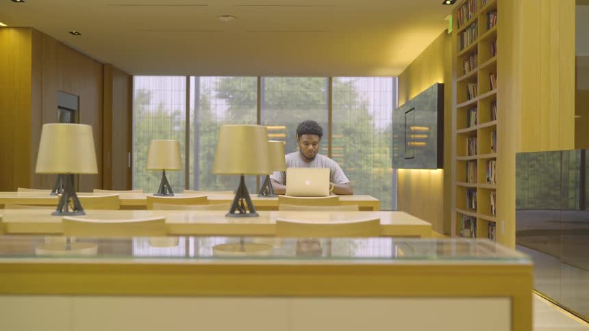 Black man sits at the table and uses laptop in office during daylight