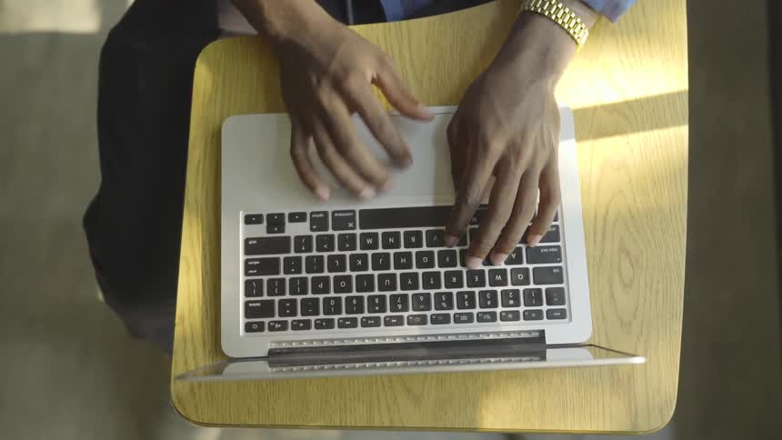 An overhead view of a man using a laptop while seated at a small desk
