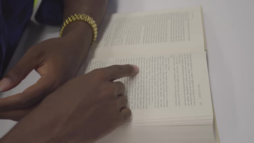 A black man moves his finger across the text in a book as he reads