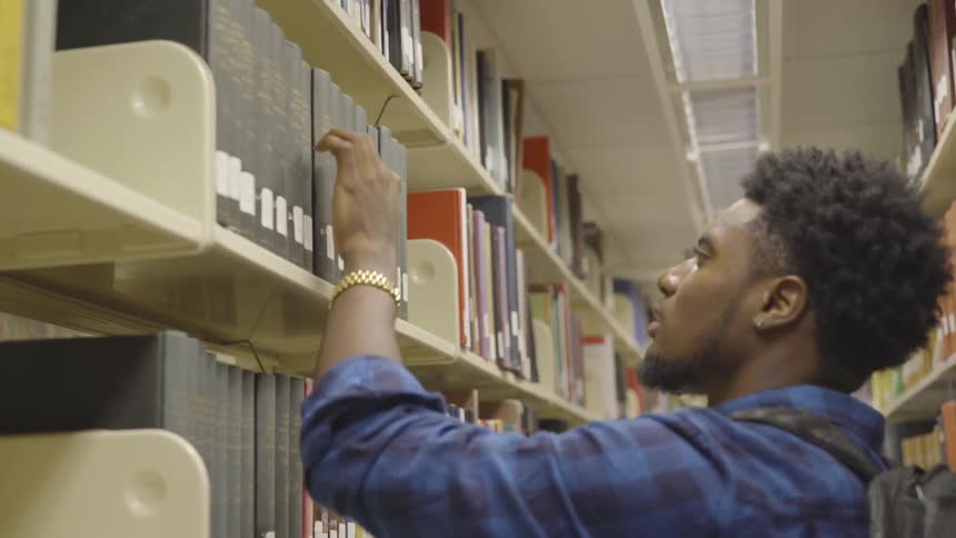 A man looks for and grabs a library book off of the shelf with his hand