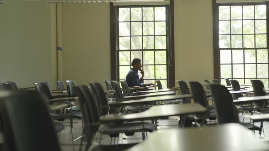 A student sits at a desk in an empty classroom