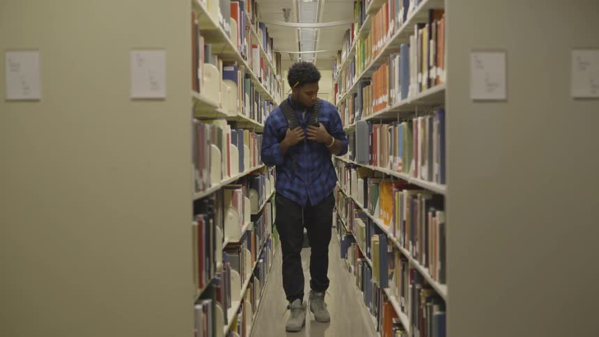 Male student walking in an aisle at the library looking for a book